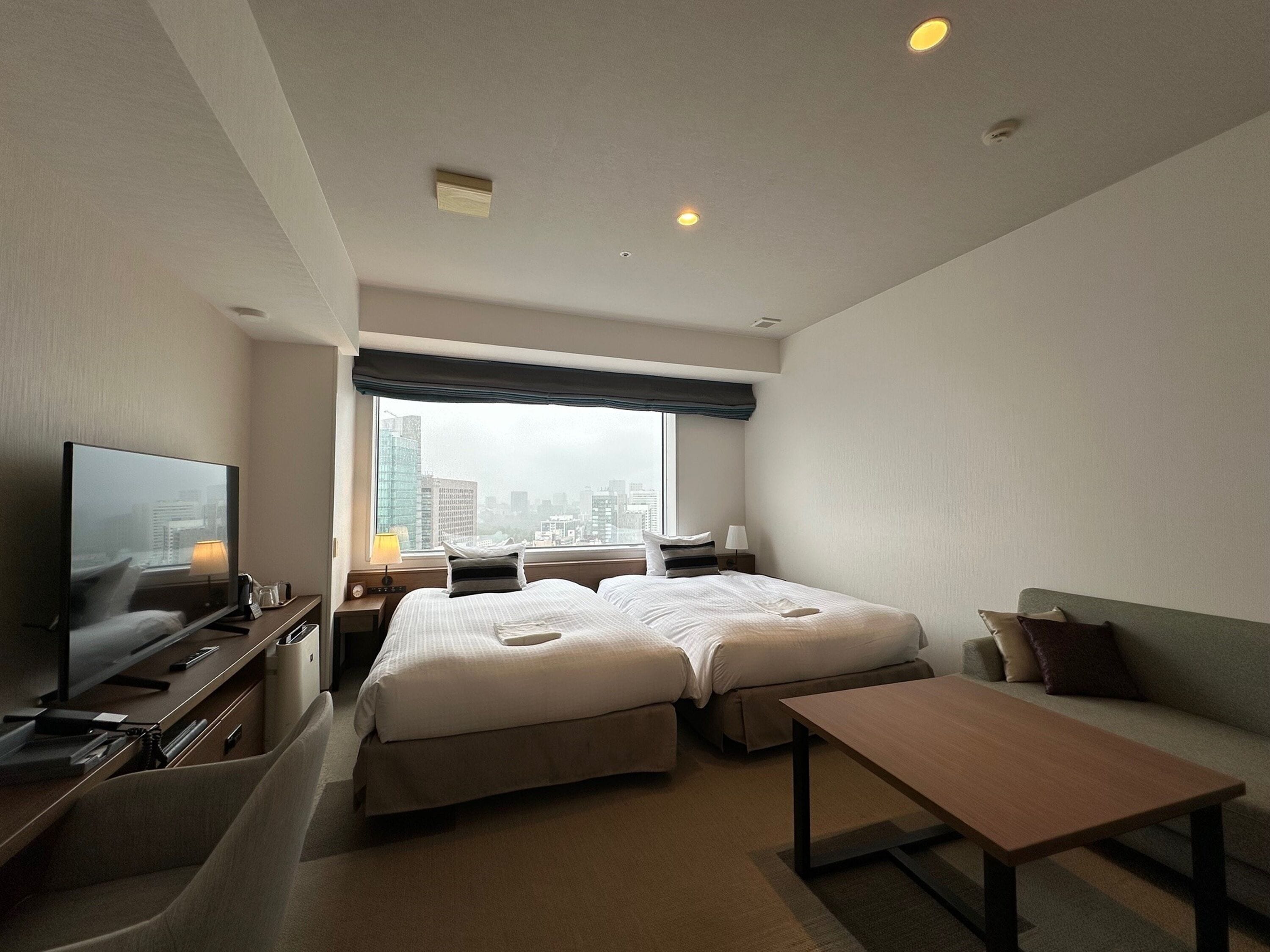 A hotel room with a large bed, a TV, a desk, and a view of the city.