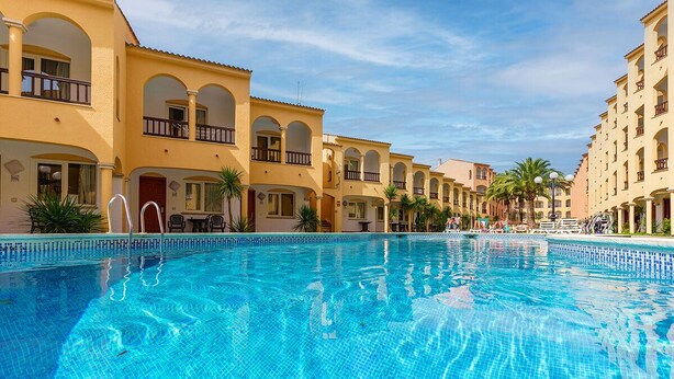 A swimming pool surrounded by multi-story buildings with balconies and palm trees.