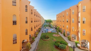 A courtyard with a central fountain, surrounded by uniform yellow buildings with arched windows and balconies.