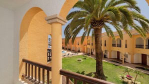 A courtyard with palm trees, a pool, and yellow buildings with arches.