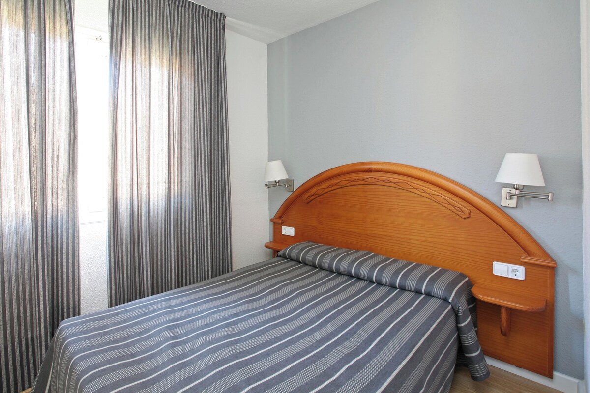A hotel room with a single bed, two bedside lamps, and a window with curtains.