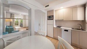 A modern kitchen with white cabinets, a microwave, a dishwasher, and a sink. There is a dining area with a white table and chairs.