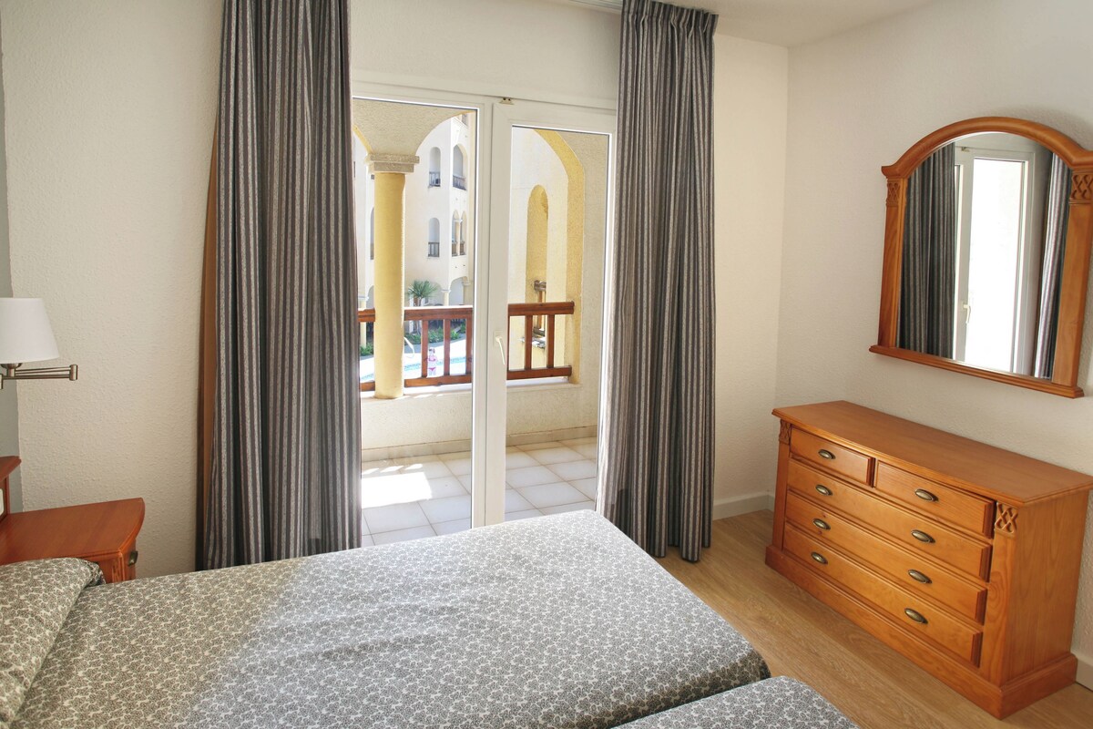 A bedroom with a bed, a wooden dresser, a mirror, and a window with curtains.
