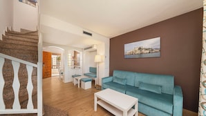 A living room with a teal sofa, a white coffee table, and a staircase leading to another room.