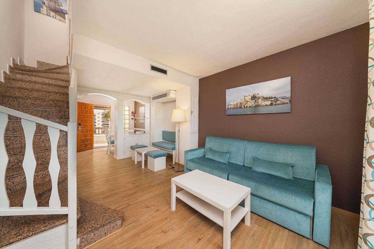 Un salon avec un canapé de couleur turquoise, une table basse blanche et un escalier menant à une autre pièce.