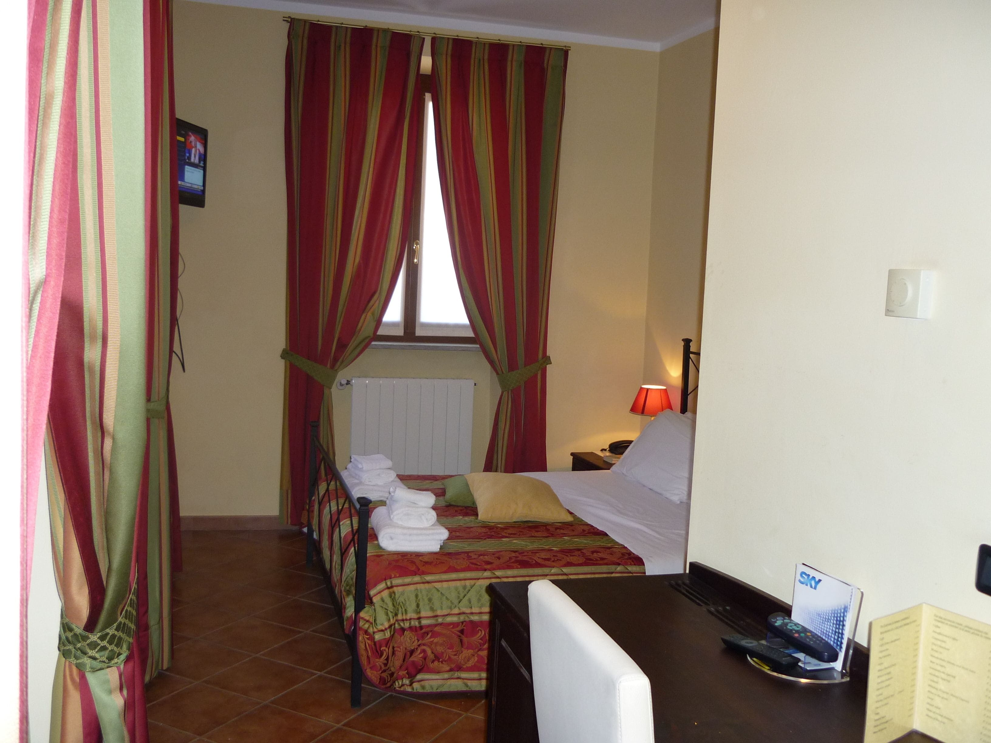 A hotel room with a bed, a desk, and a window with curtains.