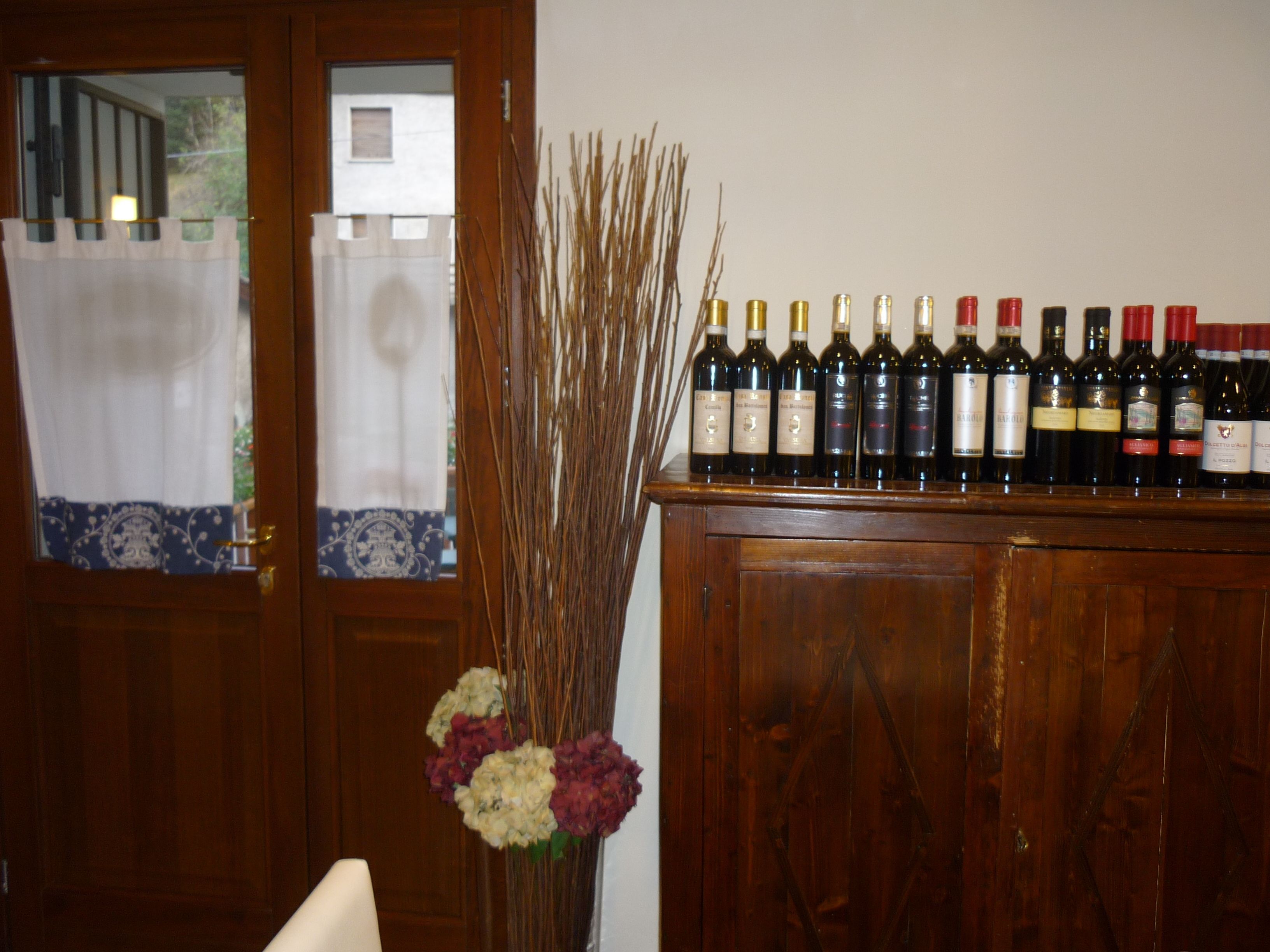 A wooden cabinet with wine bottles and a vase with dried plants.