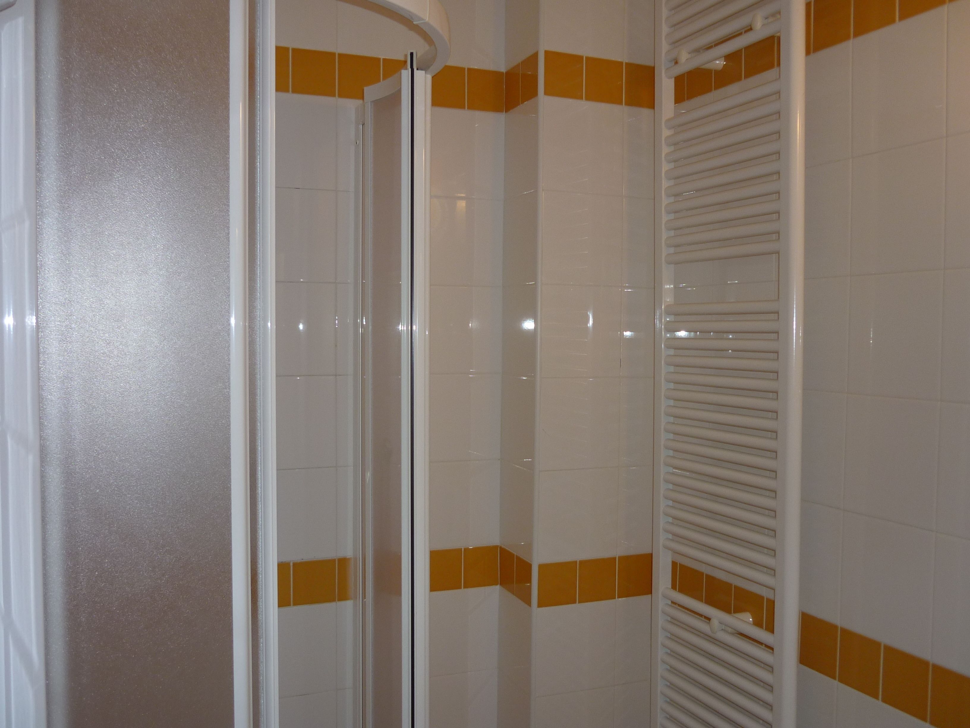A bathroom with white and orange tiles, a glass shower door, and a white towel rack.