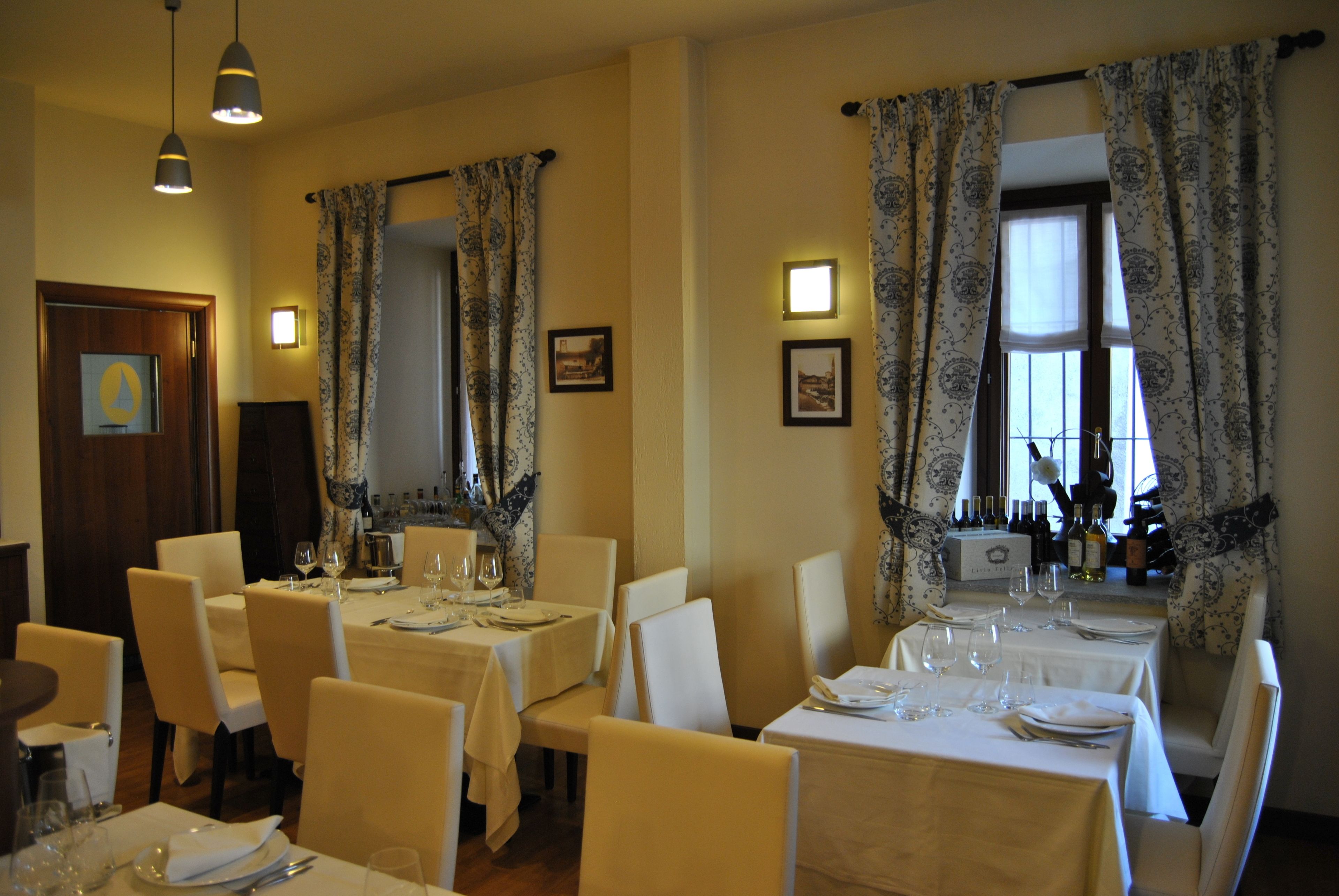 A dining area with tables set for service, featuring a classic interior design with patterned curtains and wall-mounted lighting.