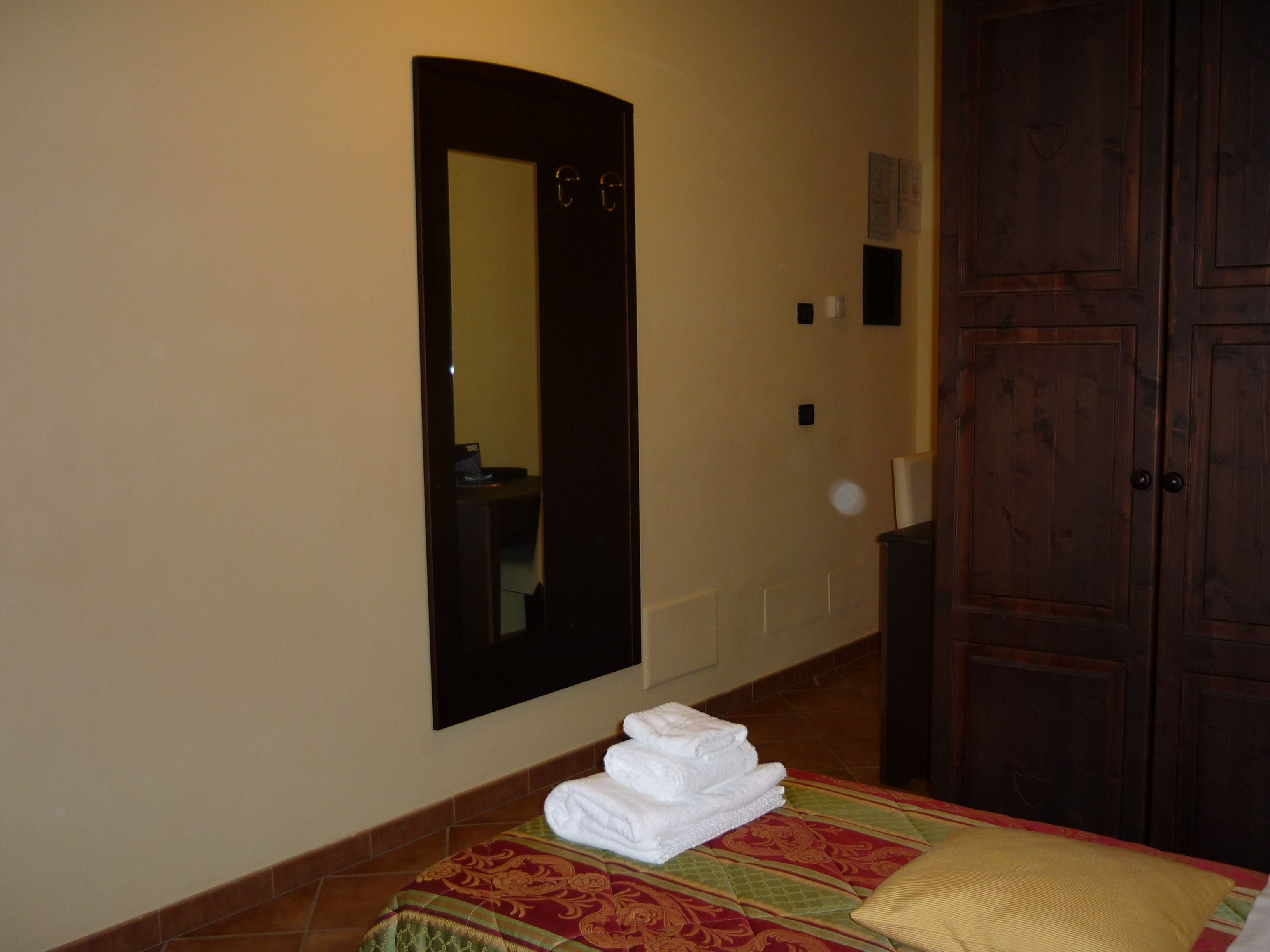 A hotel room with a bed, a folded towel stack, a mirror, and a wooden wardrobe.