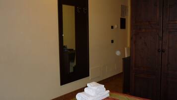 A hotel room with a bed, a folded towel stack, a mirror, and a wooden wardrobe.