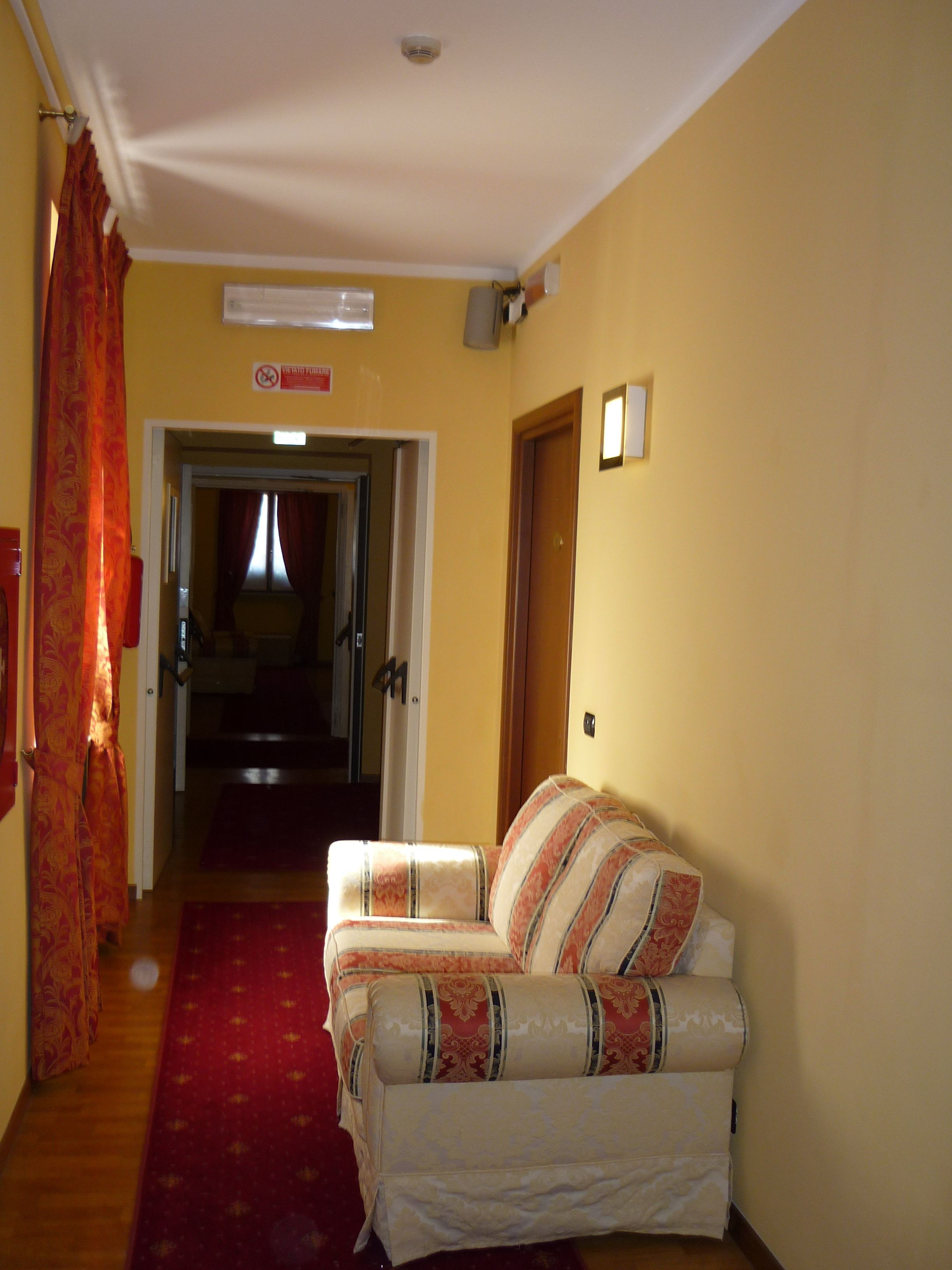 A hallway with a red carpet leading to a door, a sofa with patterned cushions, and a sign on the wall.