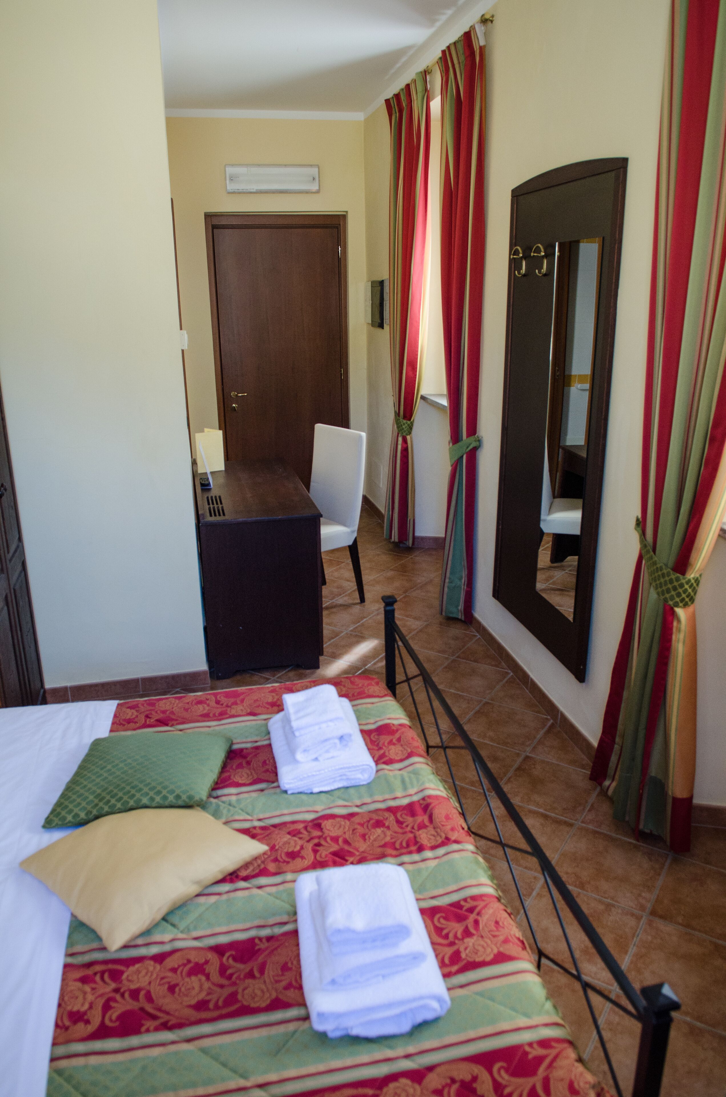 Una habitación de hotel con cama, escritorio, silla, espejo y cortinas.