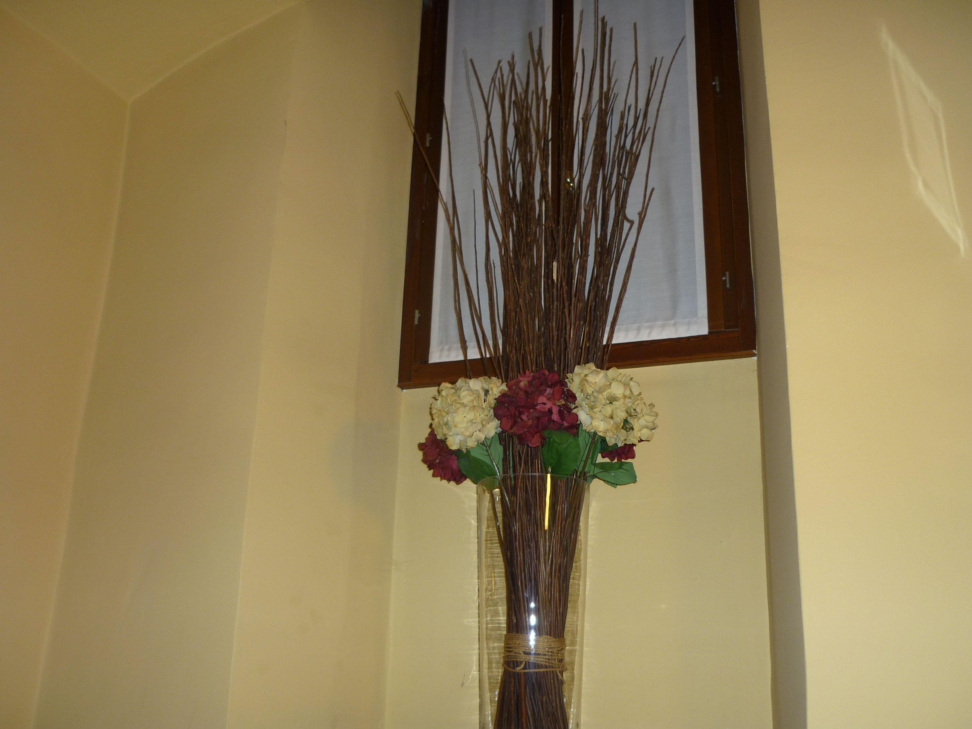 Un vase avec des fleurs et des branches, posé sur un mur.