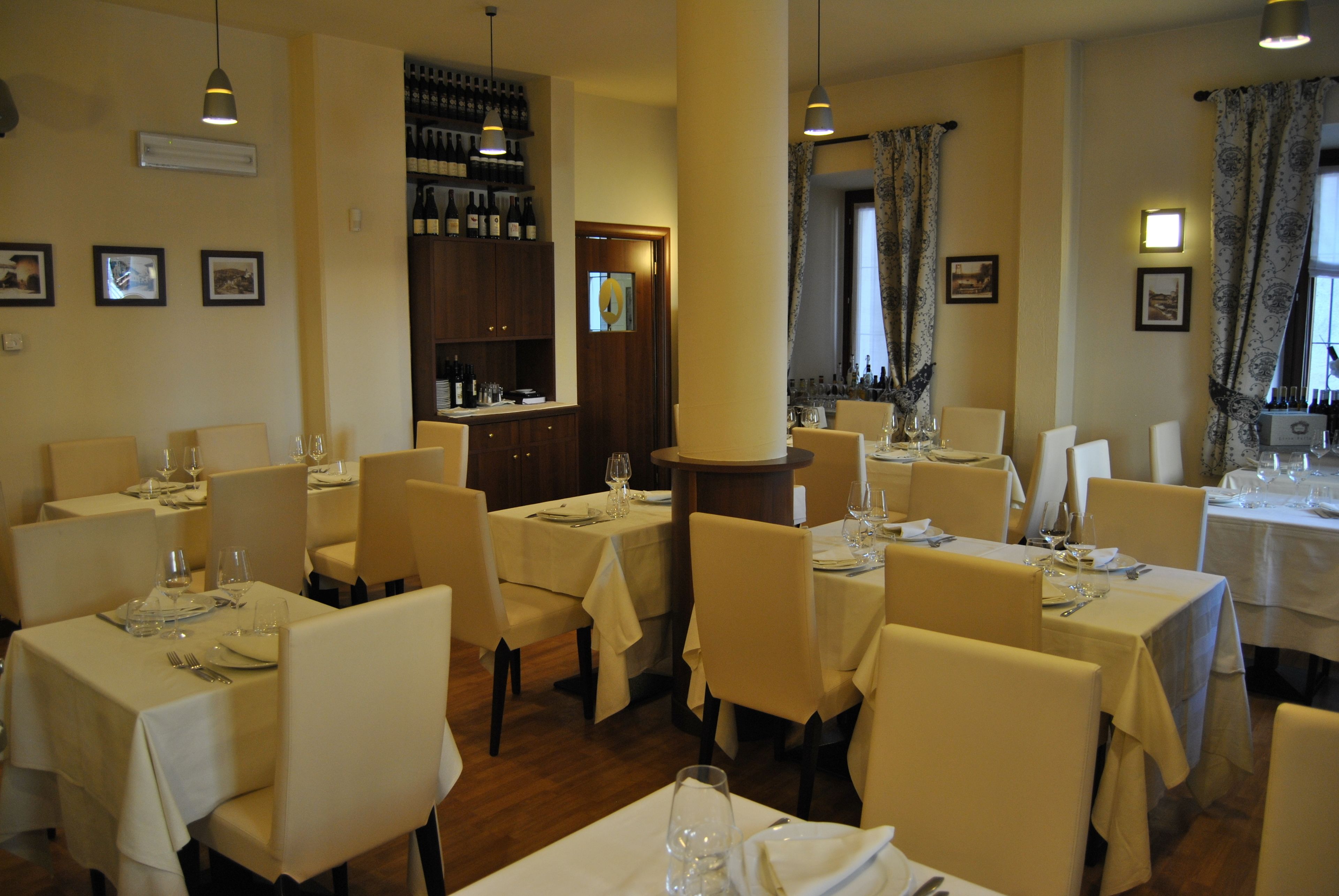 A restaurant with multiple tables set for dining, featuring a bar area with wine bottles and a wooden cabinet.