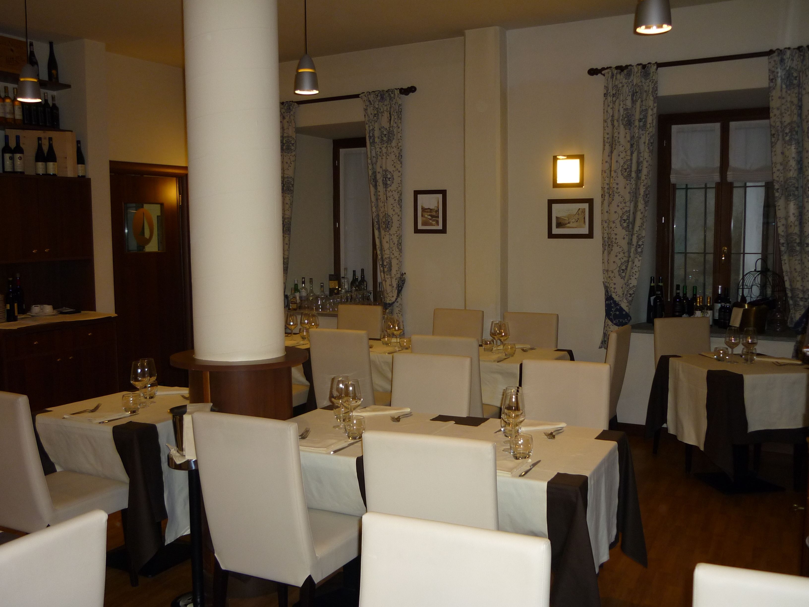 En restaurantindretning med flere borde dækket til spisning, hvide duge og stole.