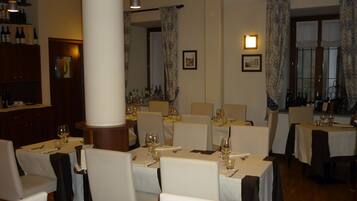 Interno di un ristorante con diversi tavoli apparecchiati per la cena, caratterizzato da tovaglie bianche e sedie.