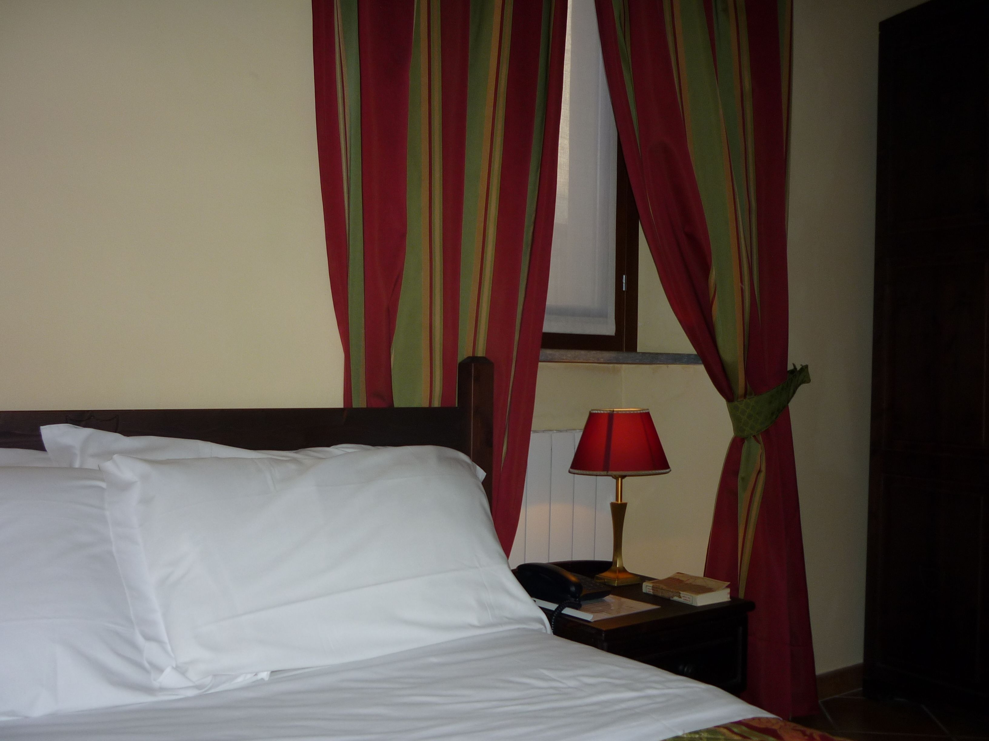 Habitación de hotel con cama, mesita de noche con lámpara y ventana con cortinas.