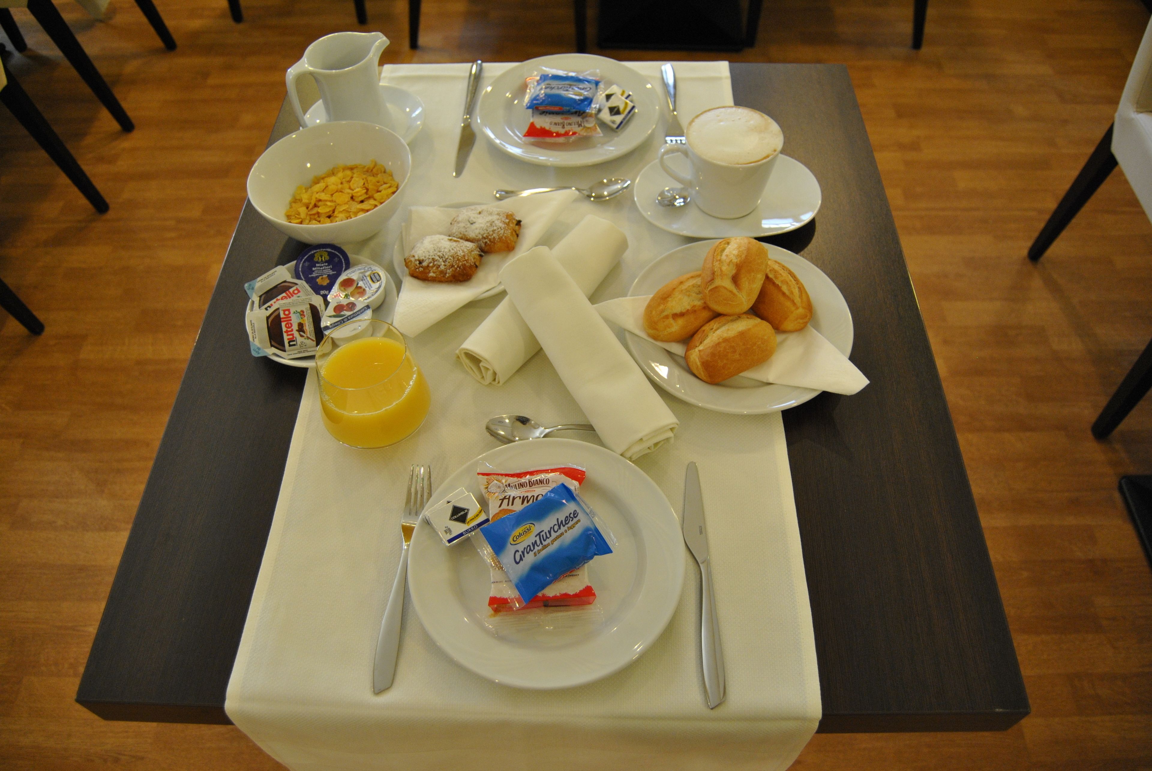 Una mesa de desayuno con un plato de pasteles, un tazón de cereal, una taza de café y un vaso de jugo de naranja.