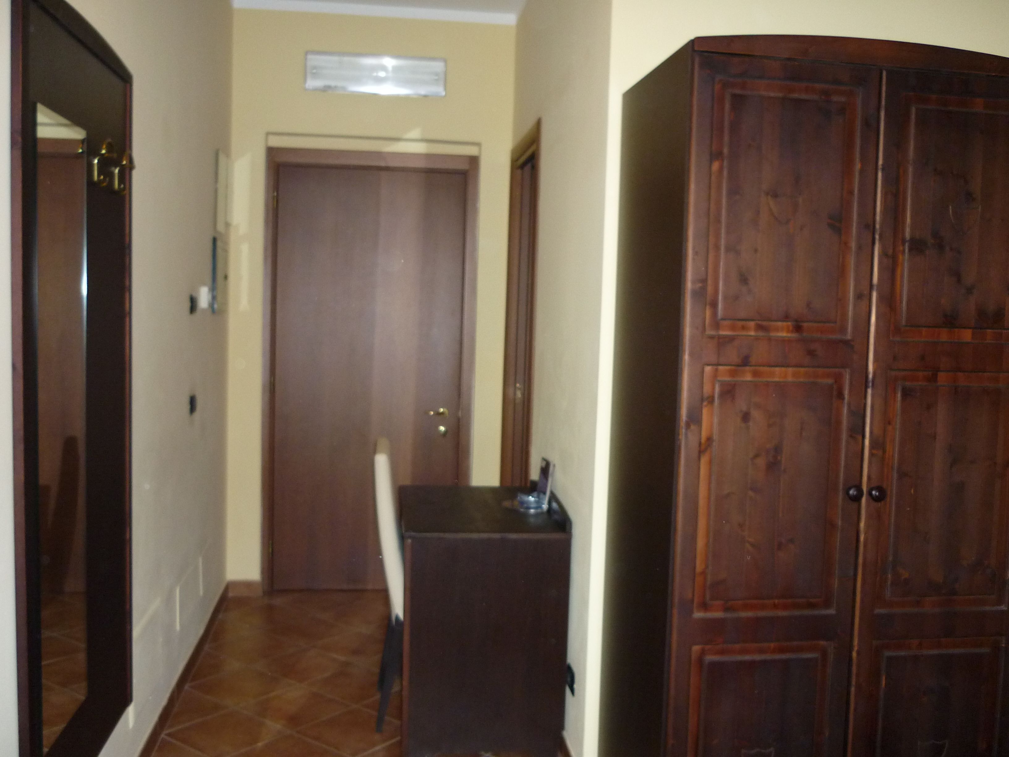 A hallway with a wooden cabinet, a closed door, and a tiled floor.