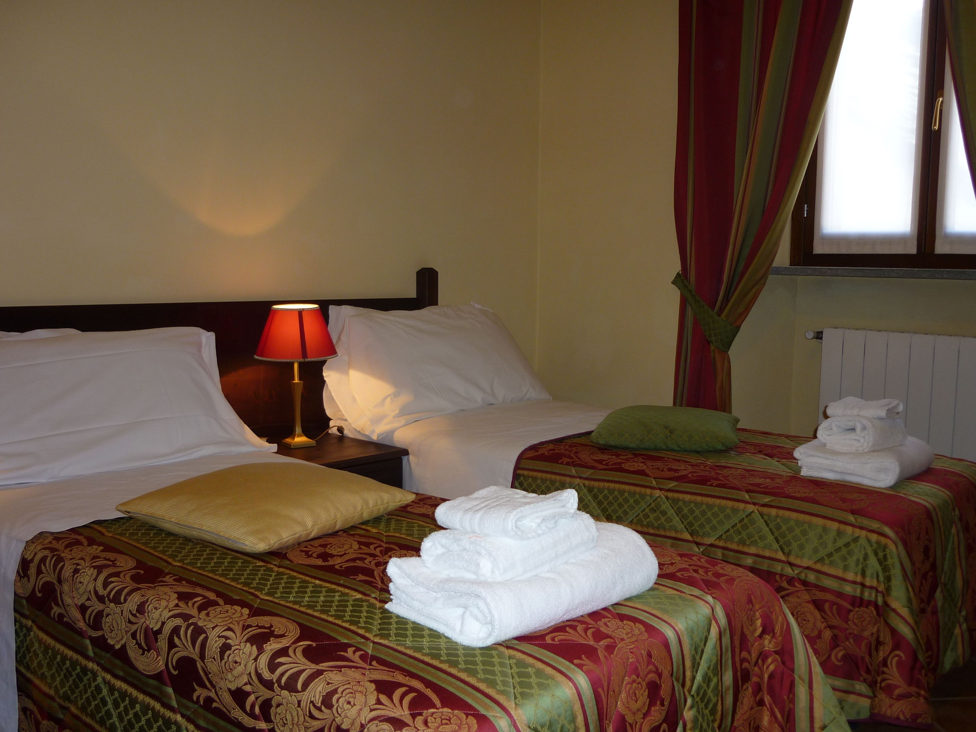 A hotel room with two beds, a nightstand, a lamp, and a window with curtains.