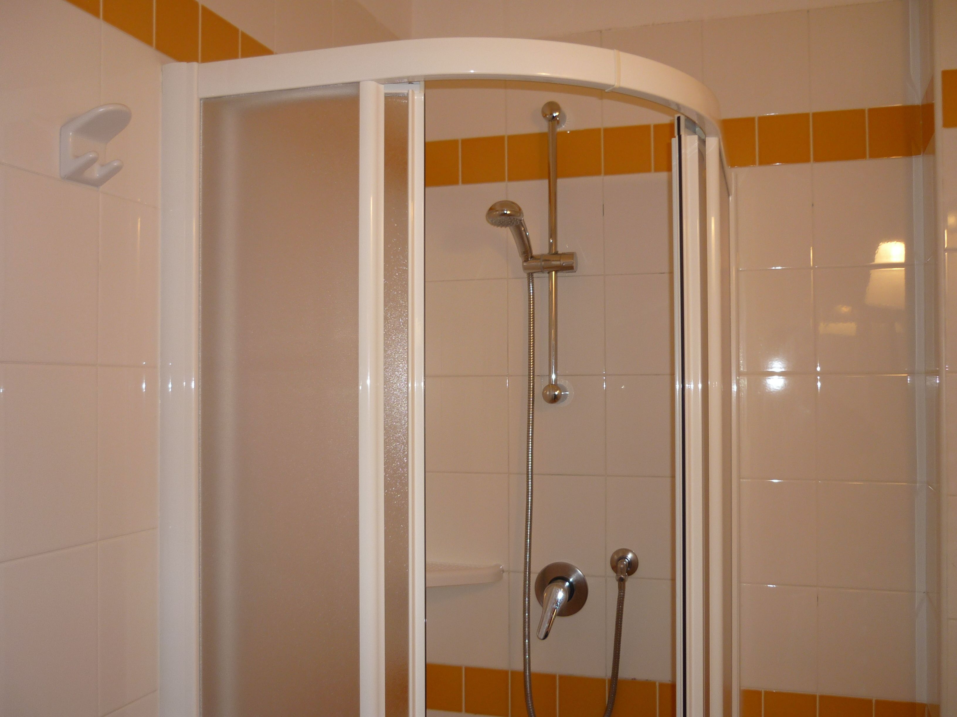 A shower enclosure with a curved door, a handheld showerhead, and a wall-mounted faucet.
