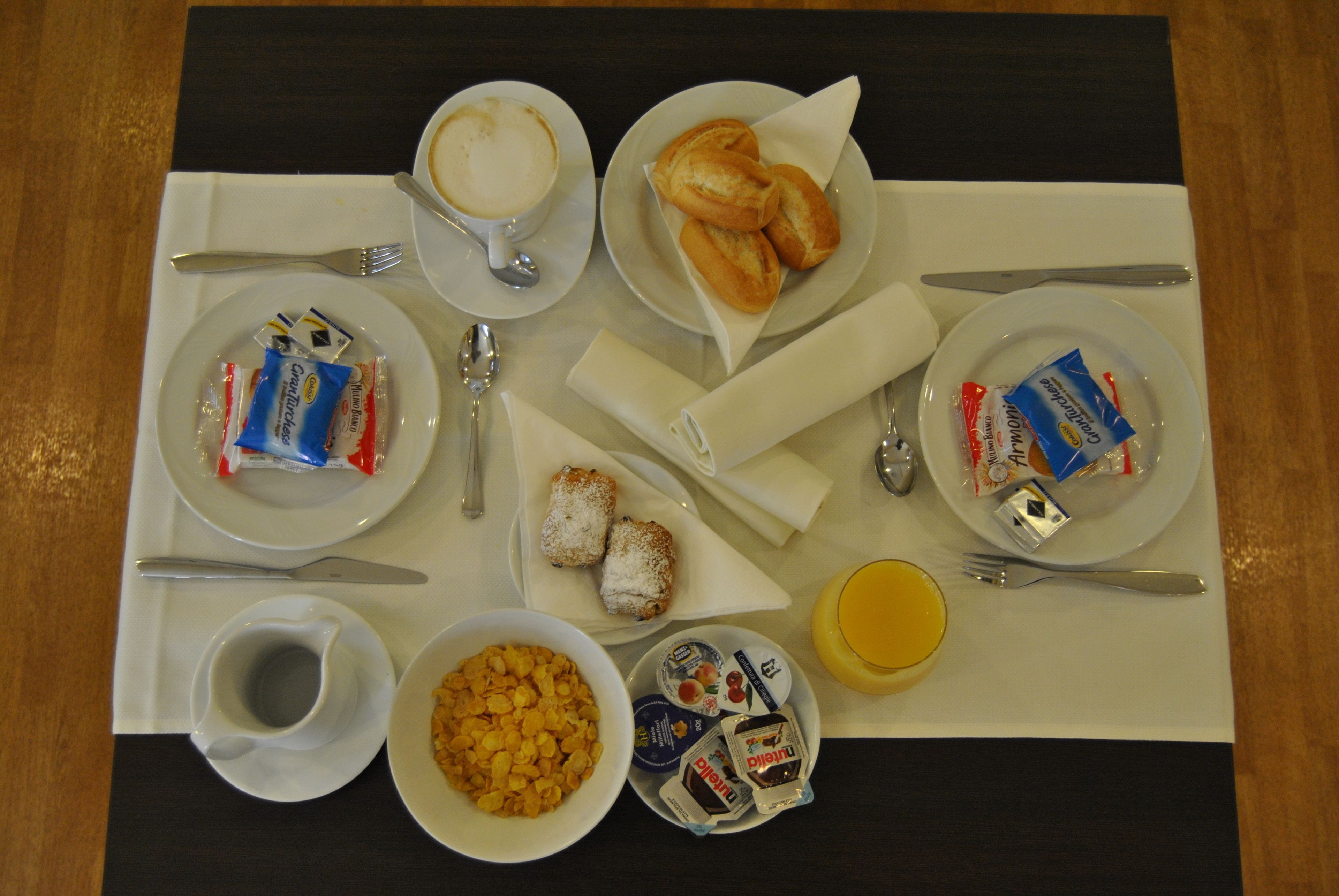 A breakfast setup with croissants, coffee, cereal, and condiments on a table.