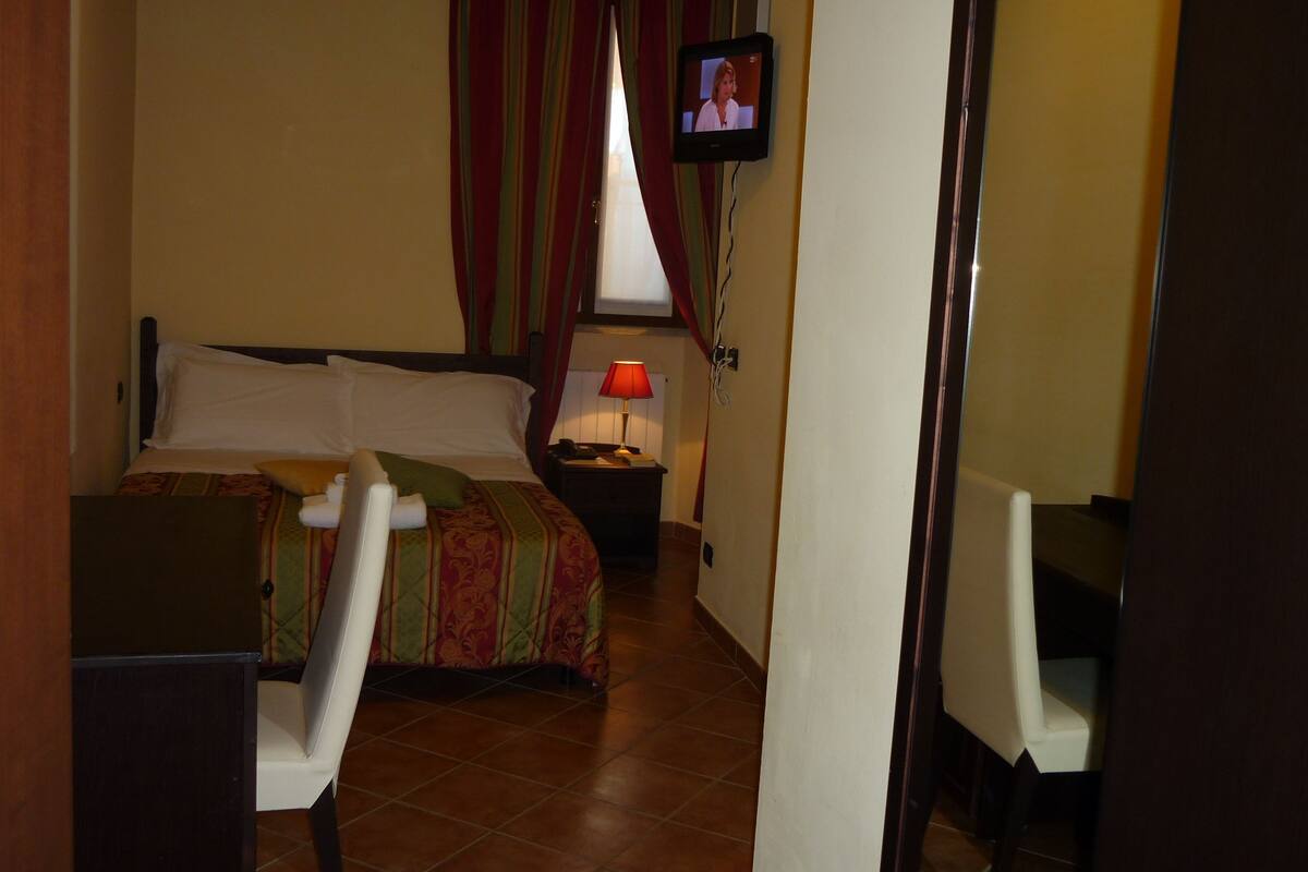 A hotel room with a bed, a desk, a chair, a TV, and a window with curtains.