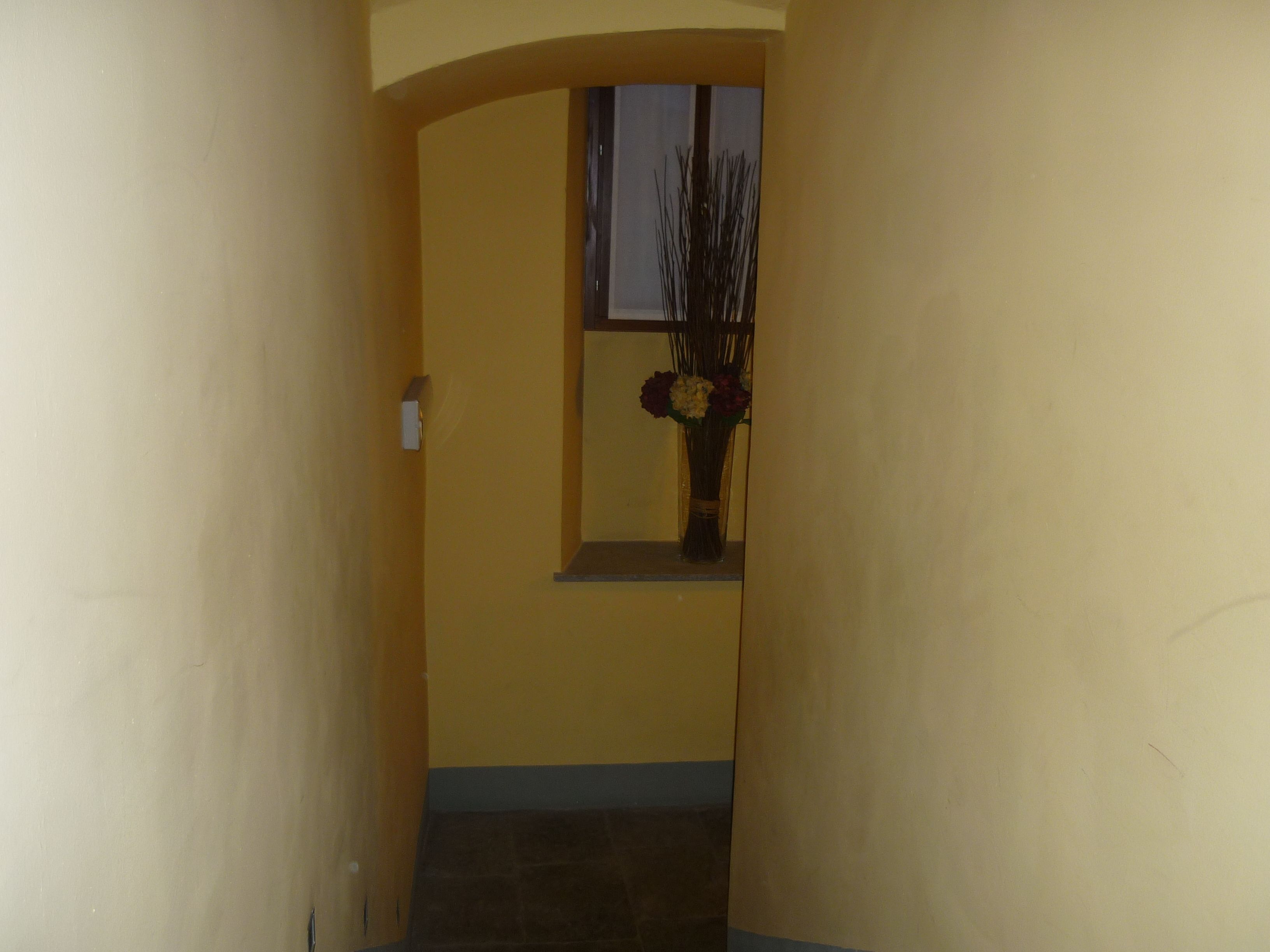 Un couloir avec une fenêtre et un vase de fleurs.
