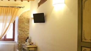 A bedroom with a bed, a television mounted on the wall, a window with curtains, and a stone wall.