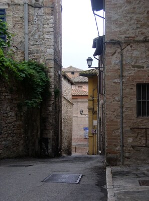 A narrow alleyway with stone walls, a metal grate on the ground, and a yellow door at the end.
