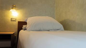 Ein ordentlich bezogenes Bett mit weißer Bettwäsche in einem Zimmer mit strukturierter Wand und einer Wandleuchte.