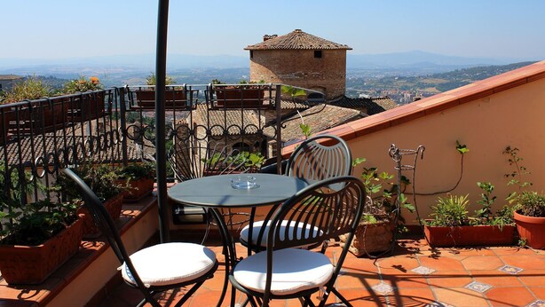 A terrace with a table and chairs, potted plants, and a view of distant buildings and mountains.