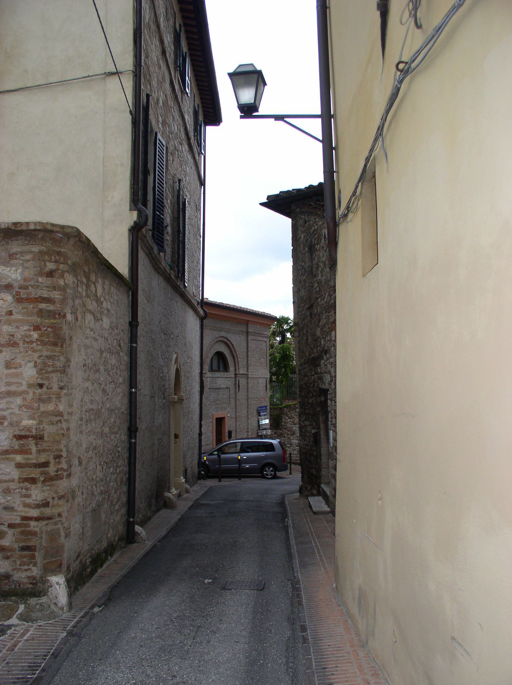 Una calle estrecha con un coche aparcado, edificios de piedra y un farol.