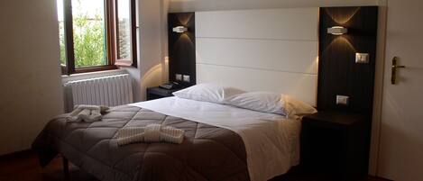 A bedroom with a bed, a window, a radiator, and two bedside tables with lamps.