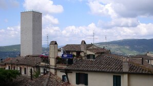 A traditional building with a prominent tower, a sign for the Primavera Mini Hotel, and a view of the surrounding hilly landscape.
