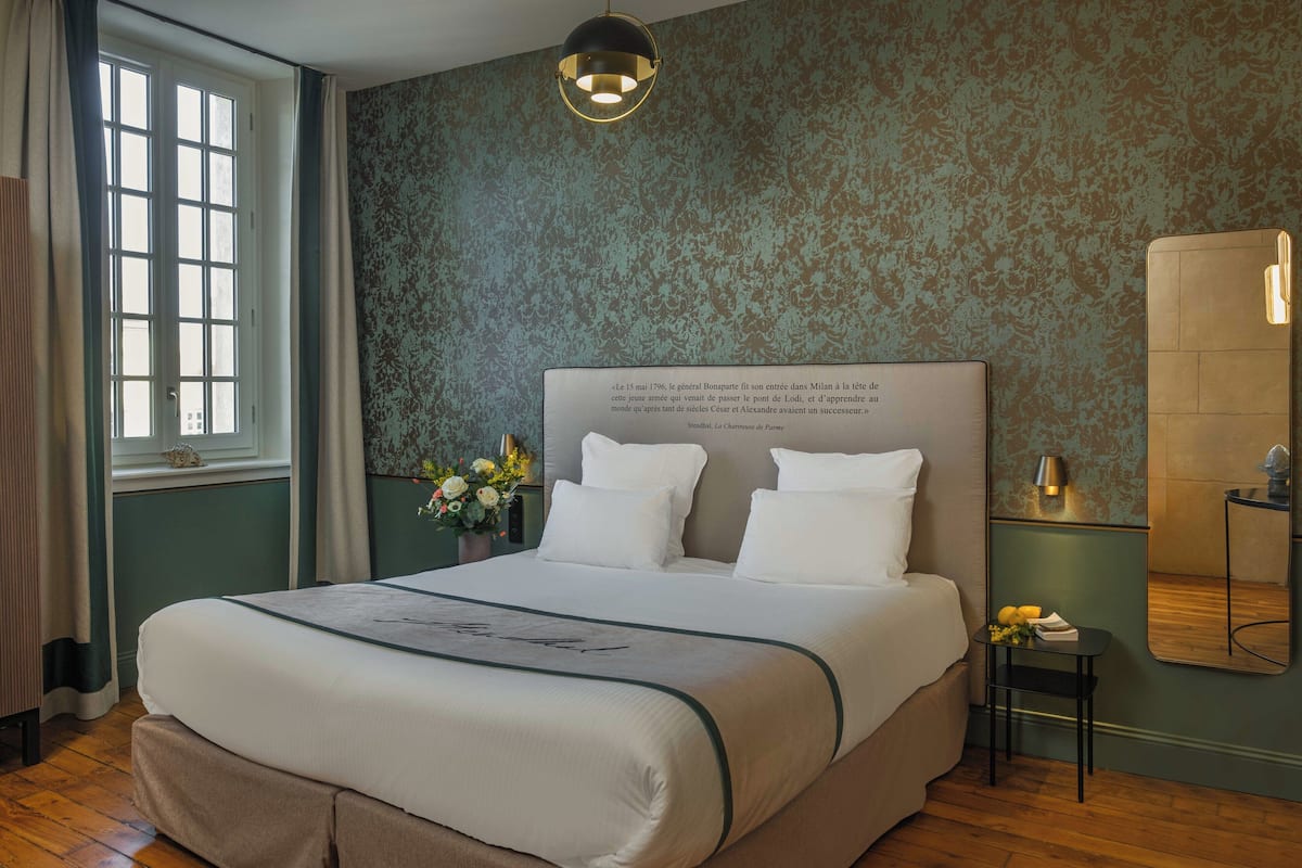 A neatly made bed with a headboard, a small bedside table with a lamp, and a window with curtains.