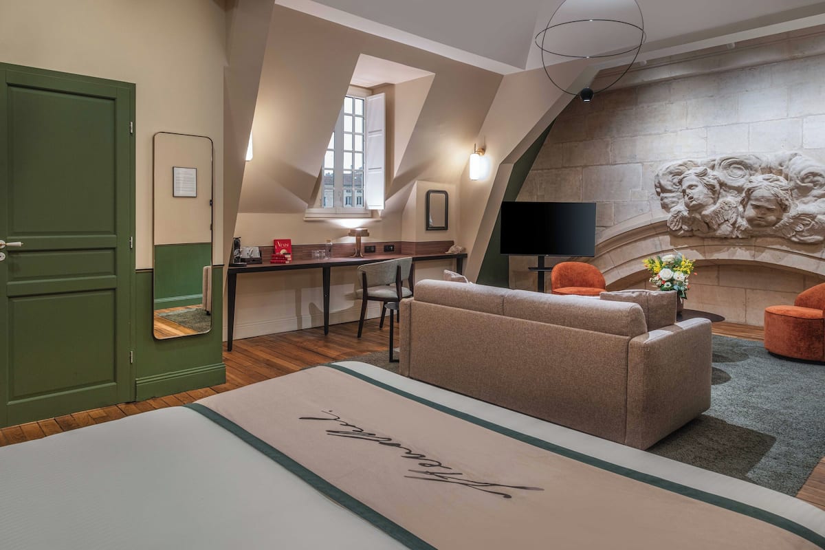 A hotel room with a bed, a desk, a TV, and a fireplace.