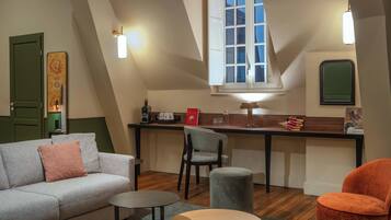 A cozy loft-style room with a sofa, a small round table, a chair, a kitchenette, and a window with a view.