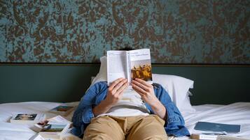 A person lying on a bed with a book open, surrounded by other books.