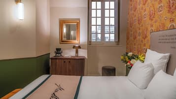 A hotel room with a bed, a wooden dresser, a mirror, a window with a view, and a wall with a patterned wallpaper.