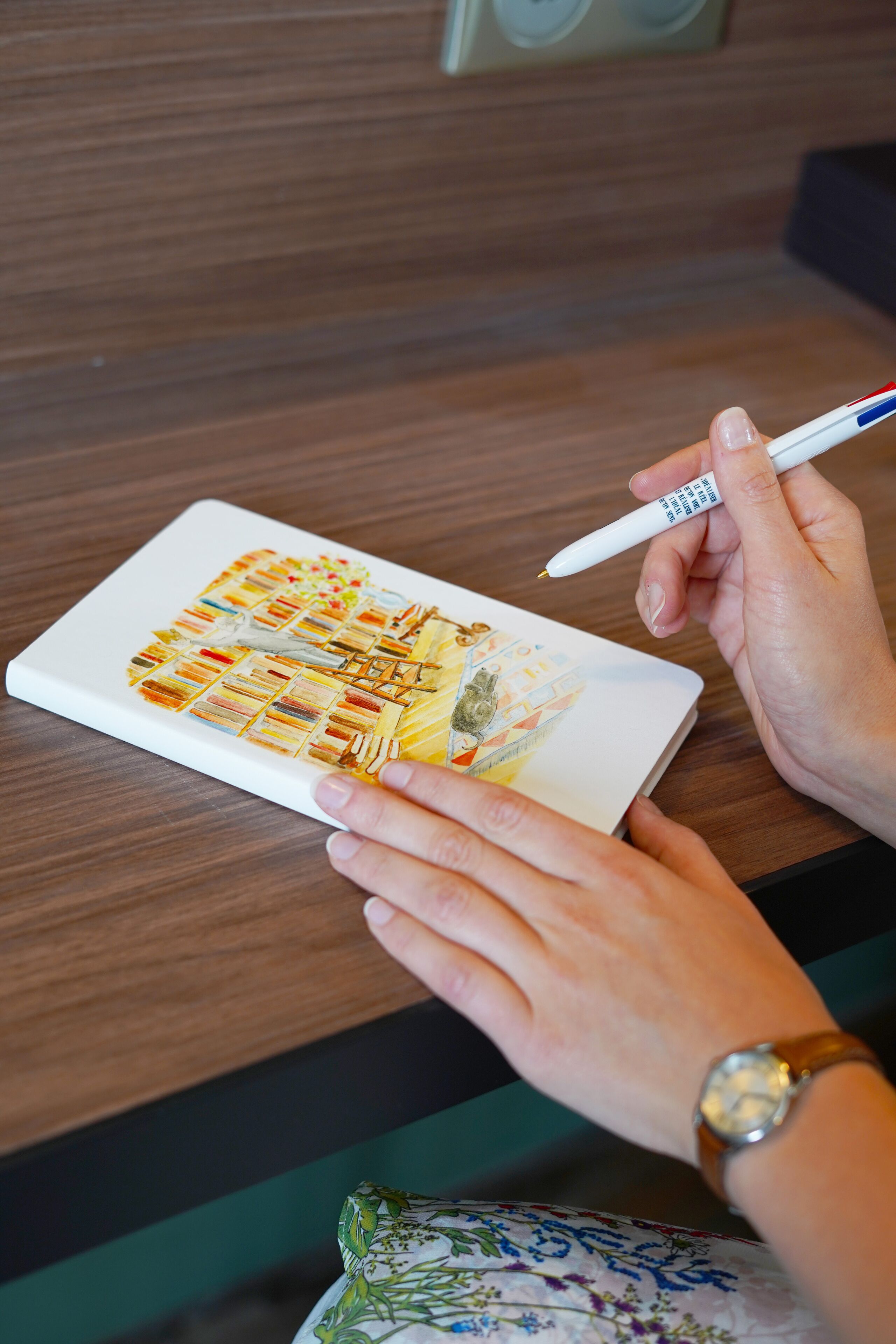 A person holding a pen over a notebook with a colorful drawing.