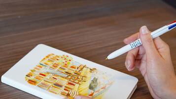A person holding a pen over a notebook with a colorful drawing.