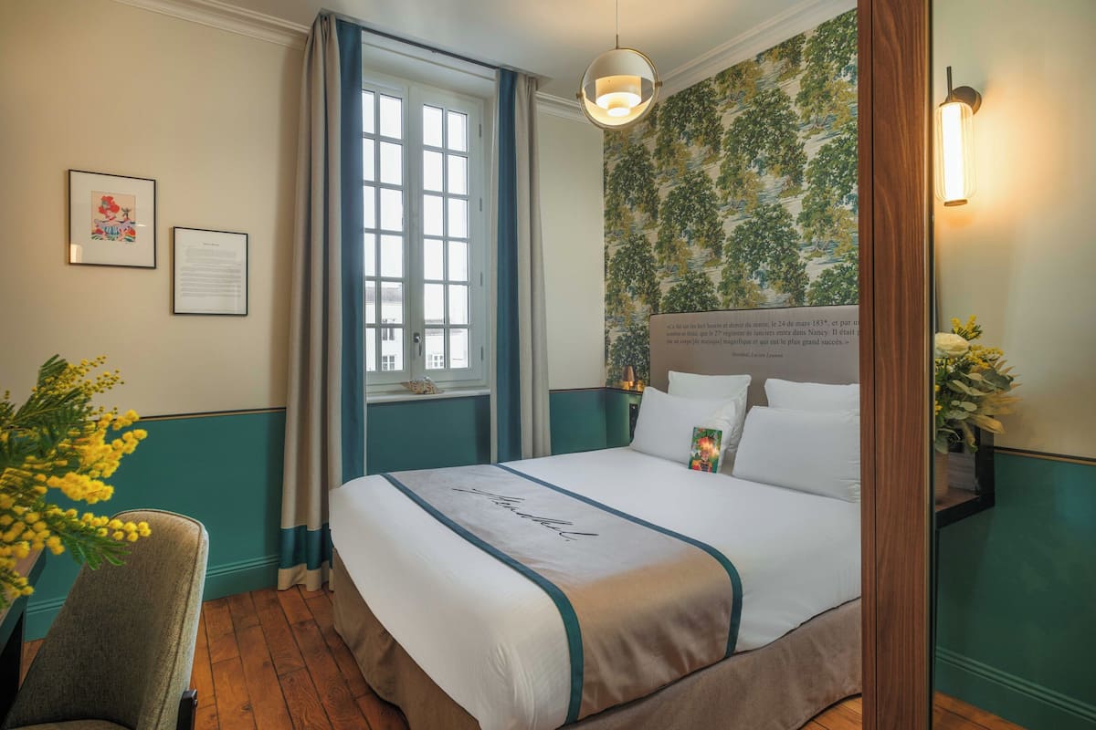 A neatly arranged hotel room with a large bed, a desk, and a window with curtains.