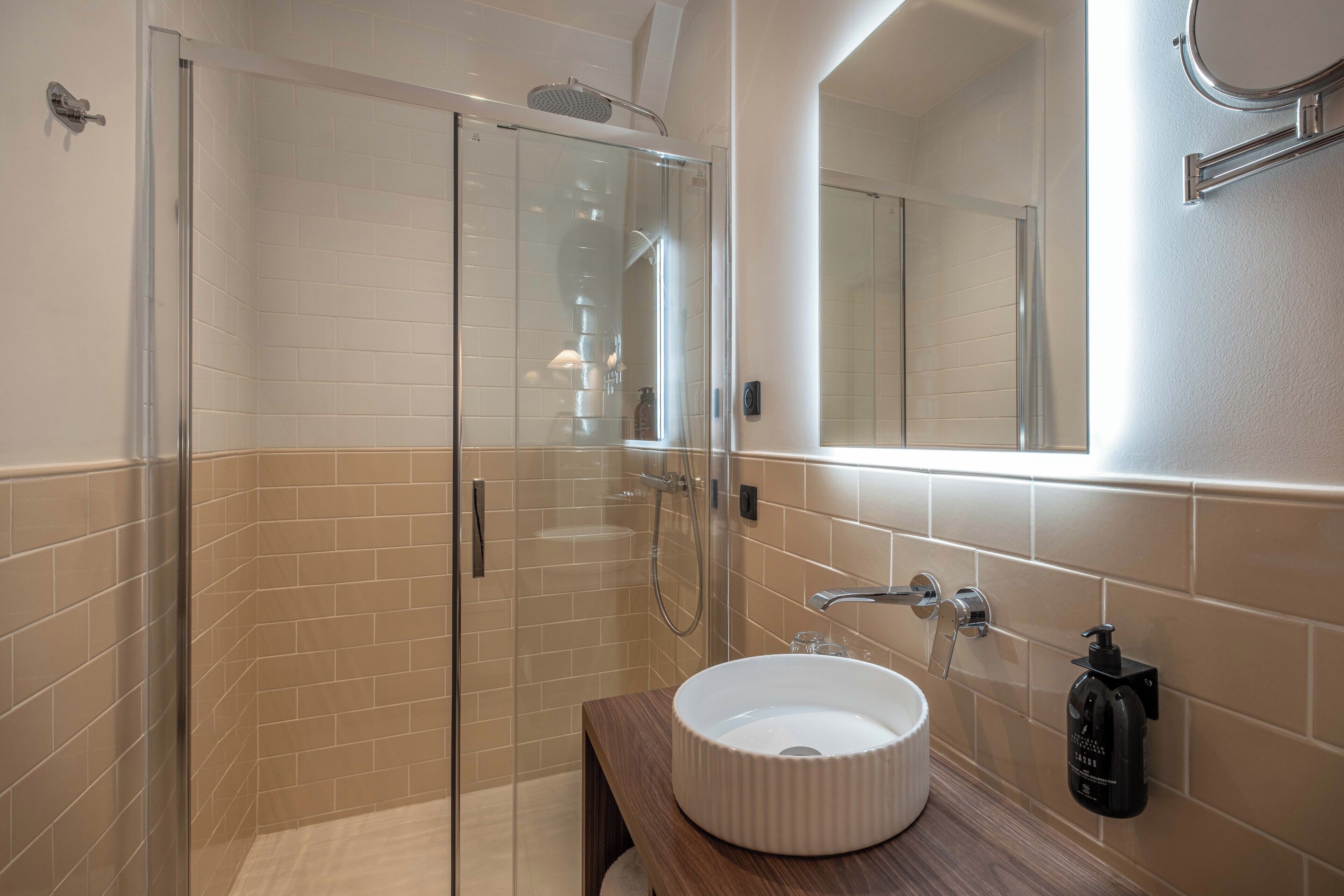 Een moderne badkamer met een douchecabine van glas, een witte wastafel en een spiegel.