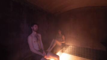 Deux personnes sont assises dans une pièce faiblement éclairée, dont le sol est recouvert de carreaux et le plafond est en bois.