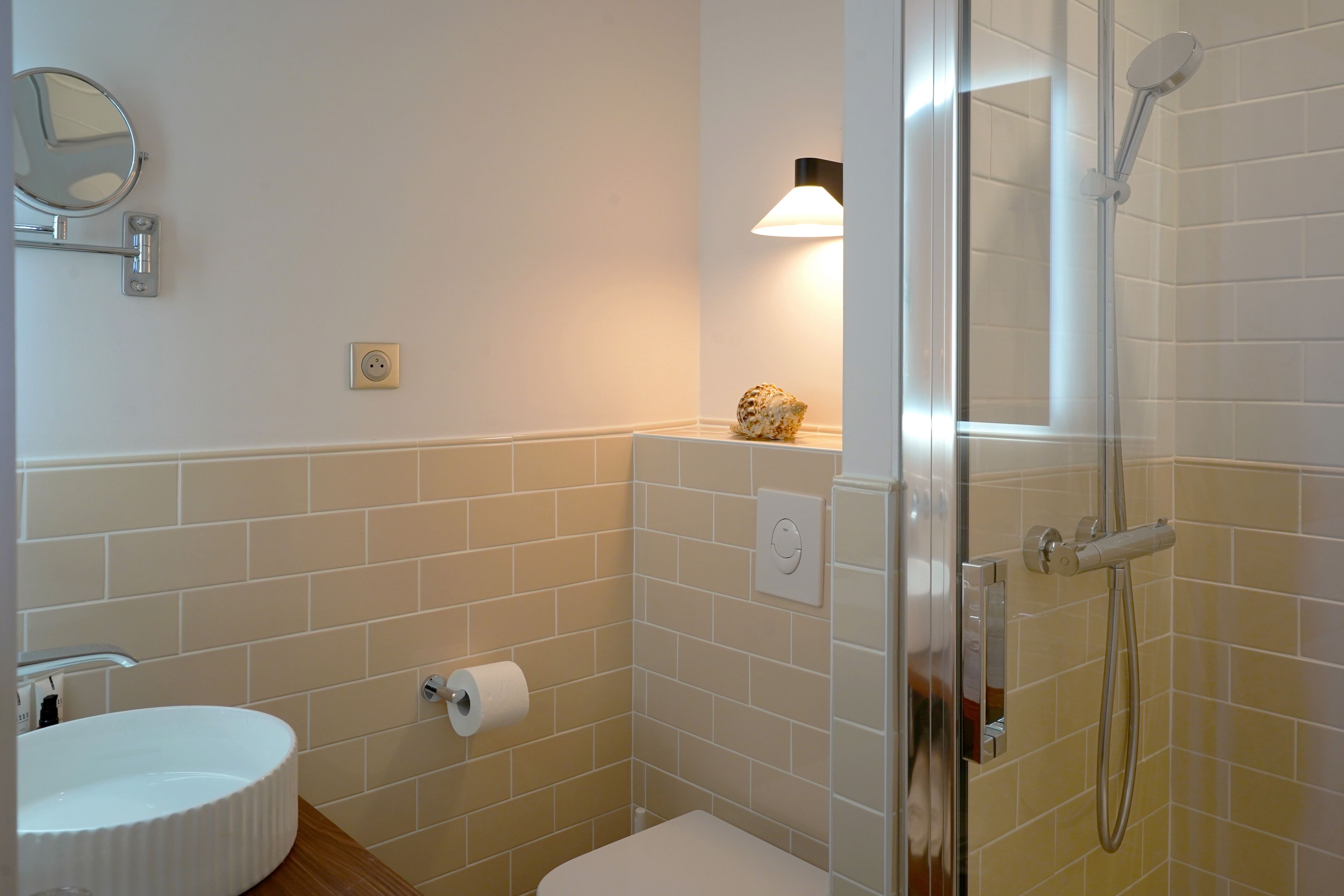 Une salle de bain équipée d’un lavabo, de toilettes, d’un miroir, d’une douche et d’un luminaire fixé au mur.