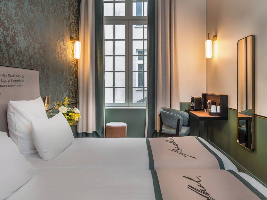 A hotel room with a bed, a desk, a chair, a TV, and a window with curtains.