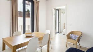 A dining area with a wooden table, white chairs, and a wicker chair with a cushion. - BcnStop Parc Güell (Barcelona)