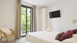 A hotel room with a bed, a chair, a TV, and a view of greenery outside. - BcnStop Parc Güell (Barcelona)